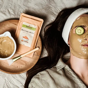 Kobieta z nałożoną ajurwedyjską maską z glinki Multani Mitti Sattva Ayurveda oraz plasterkami ogórka na oczach - głęboko regenerująca maska do kompleksowej pielęgnacji skóry