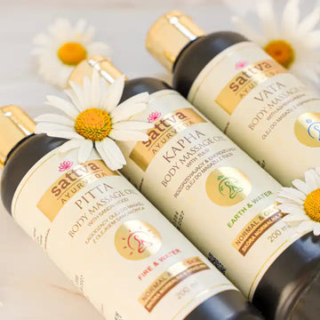 Ajurwedyjskie olejki do masażu Sattva Ayurveda (Vata, Pitta, Kapha) otoczone kwiatami rumianku - naturalna pielęgnacja ciała i dłoni według zasad ajurwedy